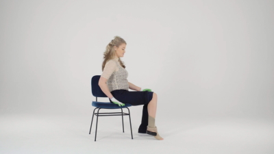 Vrouw neemt plaats op stoel met steunkous om voet en enkel.
